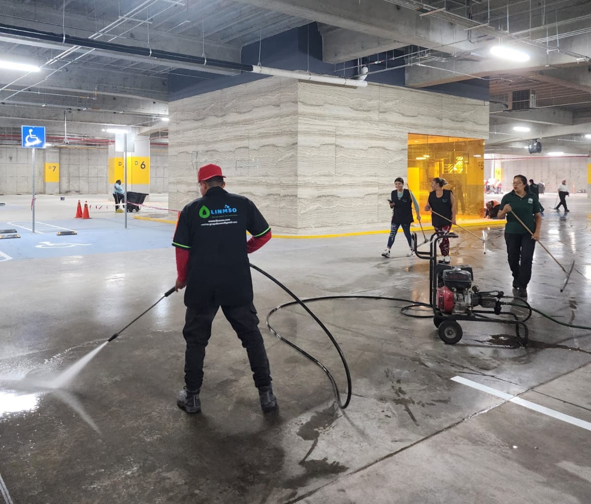 Equipo de LINMSO realizando limpieza profunda con hidrolavadora en estacionamiento industrial.